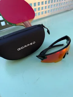 GORPED Strider sunglasses with the Ember lens next to their black GORPED case on a table tennis table
