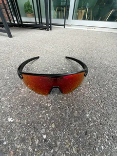 GORPED Strider sunglasses with the Ember lens lying on grey pavement outside a glass door