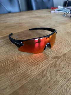 Ember sunglasses on a wooden table with red-orange reflections in the lens