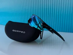 Side view of Glacier sunglasses resting on a GORPED case in front of blue glass