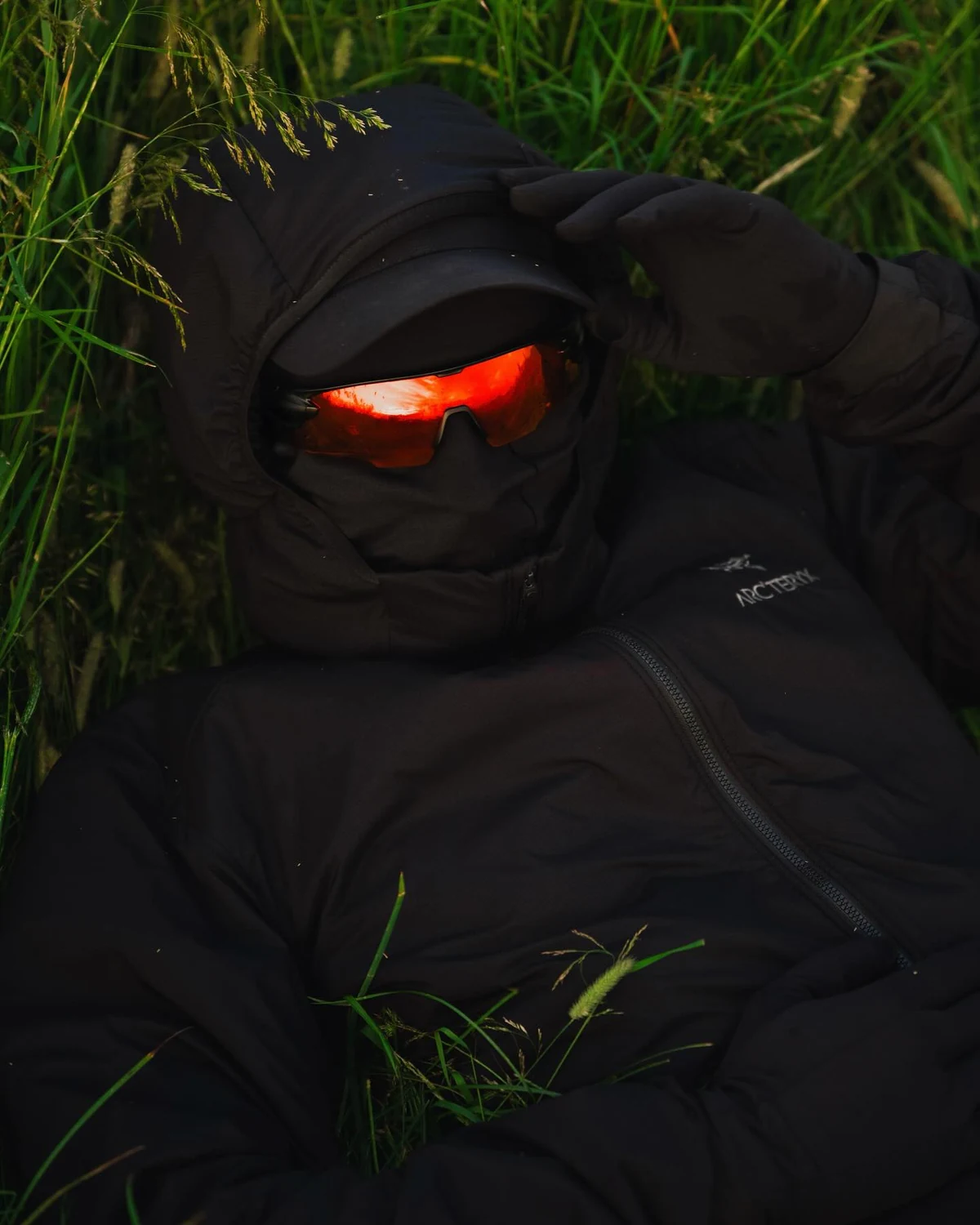 Black hood and red mirrored Strider sunglasses in tall grass, shared by @leon.helg.
