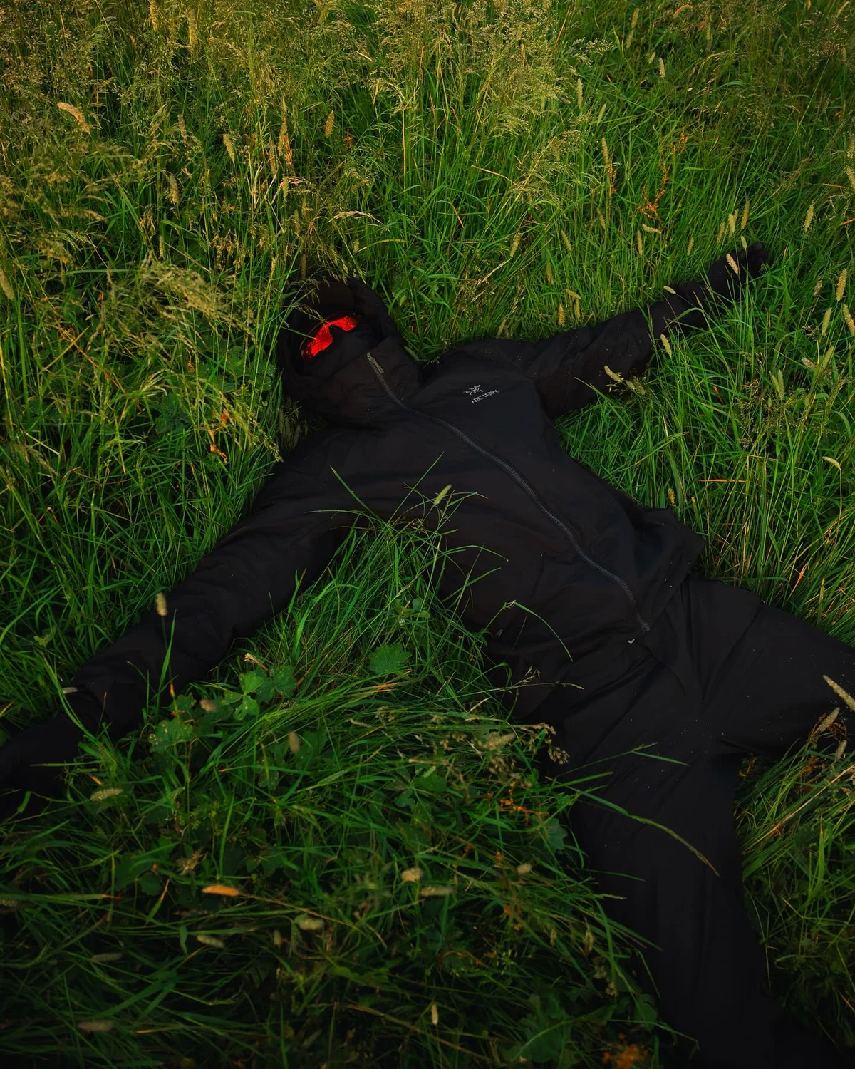 Overhead view of black outerwear and red mirrored Strider sunglasses in an alpine meadow, shared by @leon.helg.